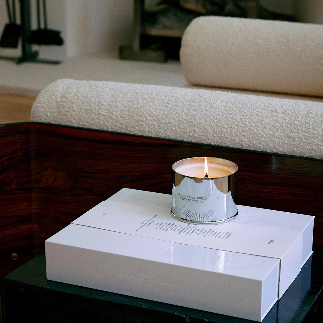 A lit silver candle resting on a white gift box on a low table.