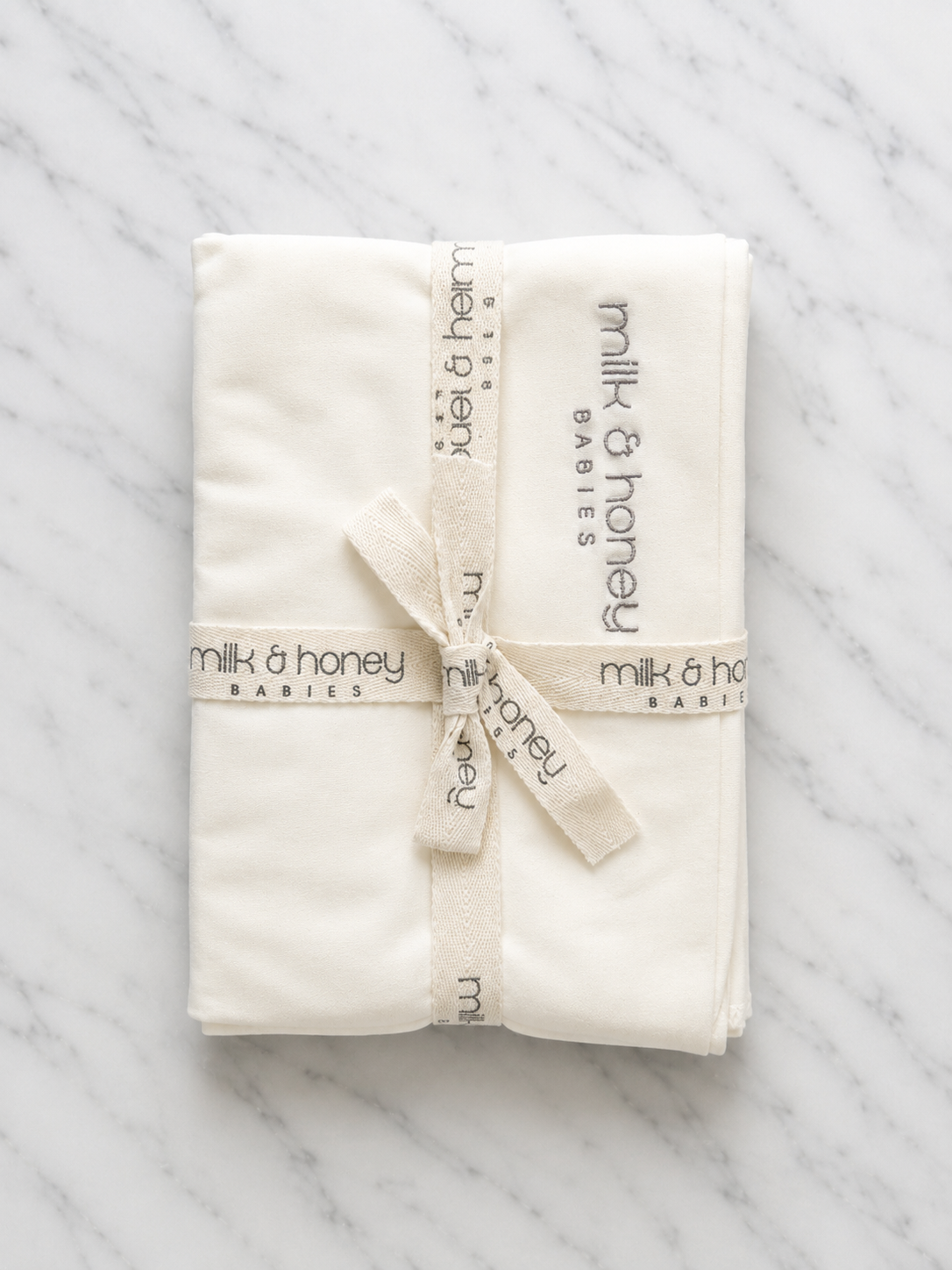 The Organic Swaddle in undyed ivory, folded and tied with milk and honey babies ribbon