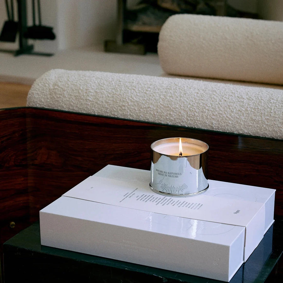 A lit silver candle resting on a white gift box on a low table.