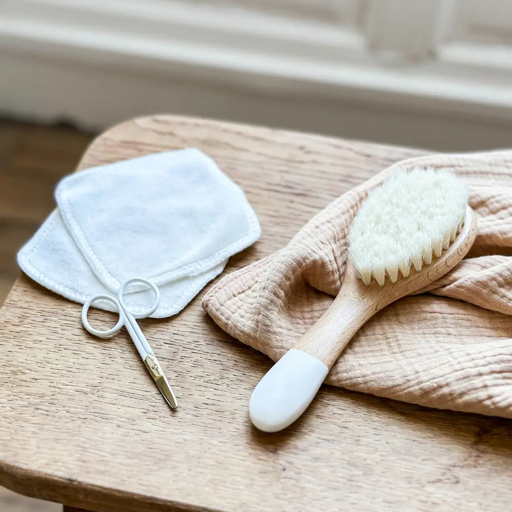 Bachca Baby Care Kit: goat-hair brush, nail scissors and cotton pads on a wood table