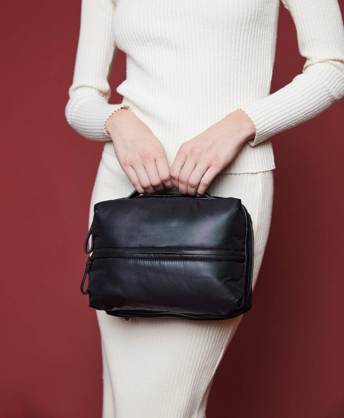 Caraa Travel Kit in Black, carried against a deep red wall